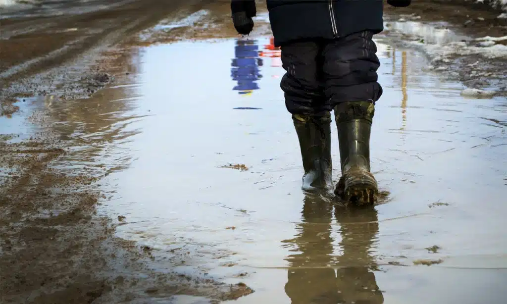 Un homme qui marche sur un terrain inondé avec des bottes de pluie