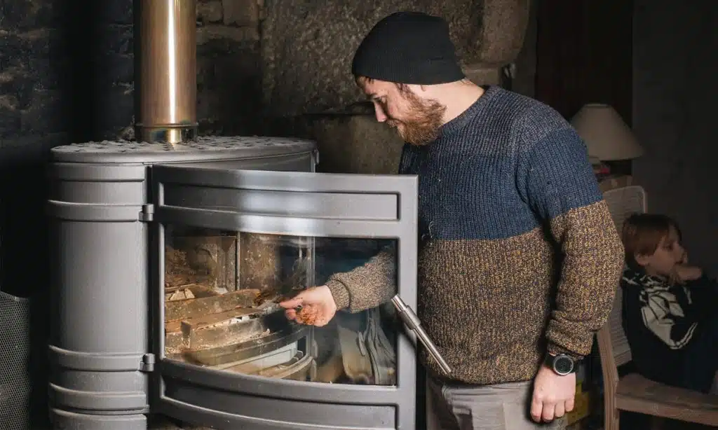 Un homme avec un bonnet allume son poêle à bois