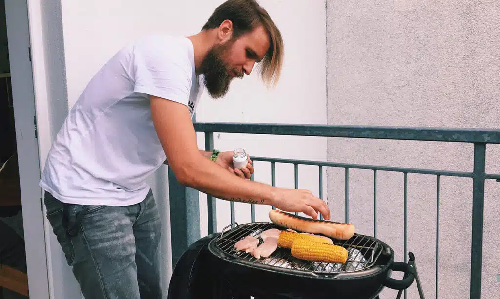 Un homme cuit des aliments dans un barbecue à charbon sur son balcon