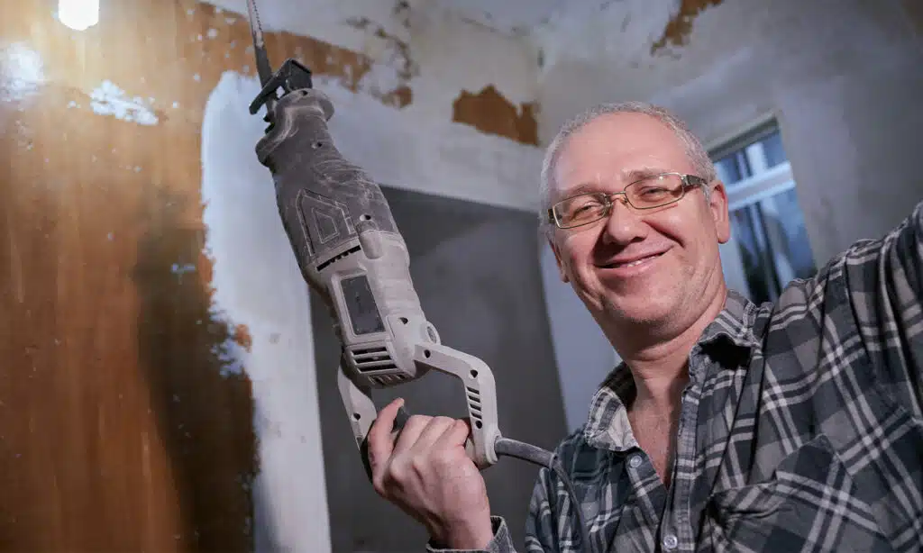 Un homme fait un selfie avec une scie électrique sur son chantier de rénovation énergétique