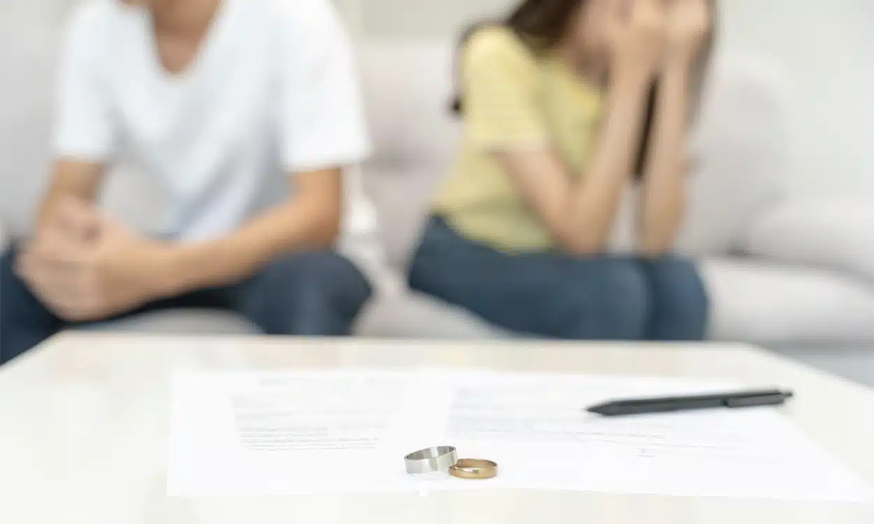 Couple qui divorce assit sur le canapé de leur appartement avec leurs alliances posées sur la table basse