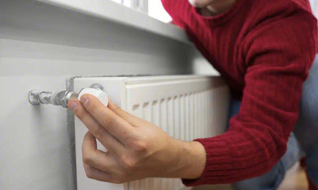 Homme en pull rouge qui règle la température de son radiateur à eau