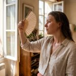 Femme s'éventant dans un appartement surchauffé en pleine canicule, logement sans protection solaire