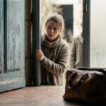 Femme mefiante entrouvrant sa porte face a un demarcheur, arnaque a la renovation