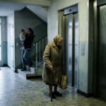 Habitante âgée devant les portes fermées d'un ascenseur en panne dans un hall d'immeuble