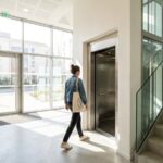 Residente marchant vers l'ascenseur dans le hall d'un immeuble avec boites aux lettres et escalier