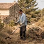 Propriétaire débroussaillant au rotofil les abords de sa maison en pierre située près d'un massif forestier classé à risque d'incendie