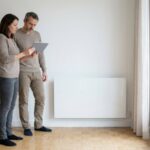 Un couple examine une tablette devant un radiateur électrique dans un logement, illustration du changement de facteur de conversion du DPE