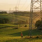 Technicien en gilet observant des pylones electriques haute tension dans la campagne francaise au coucher du soleil