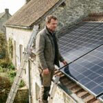 Proprietaire sur une echelle observant des panneaux solaires photovoltaiques installes sur le toit de sa maison