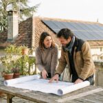 Proprietaires examinant des plans devant une maison equipee de panneaux solaires