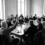 Reunion d'assemblee generale de copropriete autour d'une table, un participant leve la main pour voter