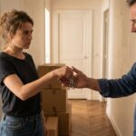 Une locataire remet le trousseau de cles a son proprietaire dans un couloir d'appartement rempli de cartons de demenagement