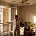 Femme ouvrant les volets d'un appartement sous la chaleur estivale, ventilateur de plafond, precarite energetique d'ete