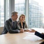 Couple d'investisseurs en rendez-vous avec une conseillere en gestion de patrimoine, tours de bureaux franciliens en arriere-plan, SCPI Elysees Pierre