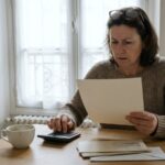 Femme assise a la table de sa cuisine, calculatrice a la main, examinant un courrier, illustration de l inflation d aout 2026 et de la revision des loyers