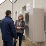 Un installateur explique le fonctionnement d une pompe a chaleur air eau a une proprietaire devant sa maison