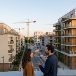 Couple d'acheteurs discutant devant des immeubles neufs, illustrant les écarts de prix de l'immobilier neuf par ville en 2026
