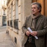 Propriétaire bailleur pensif devant l'entrée d'un immeuble parisien, trousseau de clés et bail à la main
